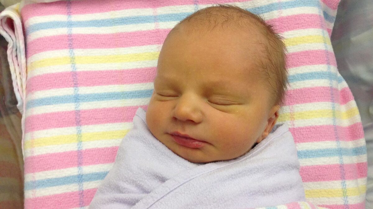 A newborn baby sleeping, swaddled in a blanket, lying on pink, blue, yellow and white striped hospital linen
